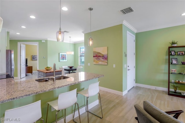 kitchen with sink, a kitchen breakfast bar, light stone counters, stainless steel fridge, and pendant lighting