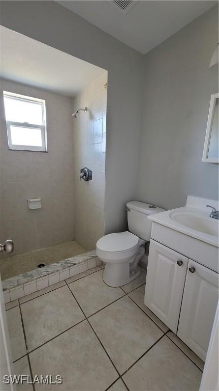 bathroom featuring tile patterned floors, vanity, toilet, and a tile shower