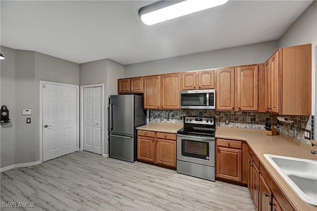 kitchen featuring decorative backsplash, appliances with stainless steel finishes, light wood-type flooring, and sink