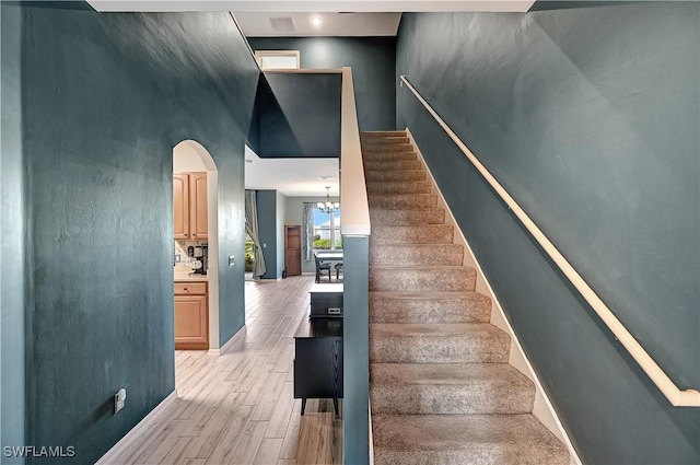 stairway with wood-type flooring, an inviting chandelier, and a high ceiling