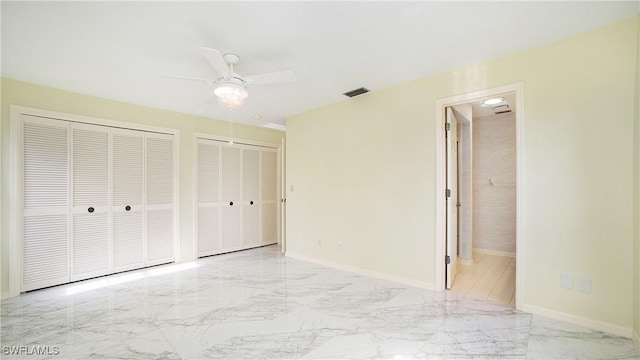 unfurnished bedroom with ensuite bath, ceiling fan, and two closets