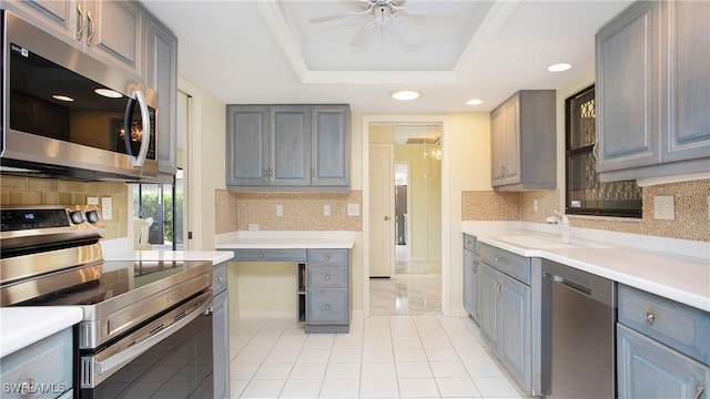 kitchen with sink, ceiling fan, appliances with stainless steel finishes, gray cabinetry, and a tray ceiling