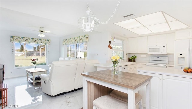 kitchen featuring ceiling fan with notable chandelier, white appliances, white cabinetry, and a breakfast bar