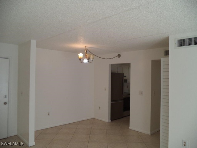 spare room featuring light tile patterned flooring, a textured ceiling, and an inviting chandelier