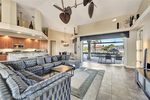 tiled living room featuring ceiling fan with notable chandelier and a high ceiling