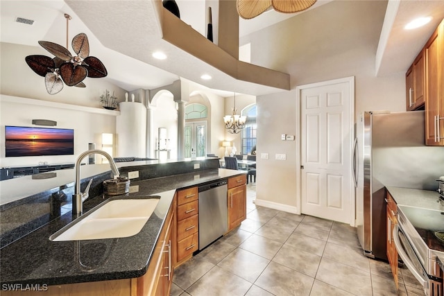 kitchen with dark stone countertops, sink, appliances with stainless steel finishes, an island with sink, and ceiling fan with notable chandelier