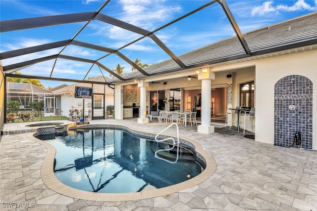 view of pool featuring glass enclosure, a bar, a patio area, exterior kitchen, and an in ground hot tub