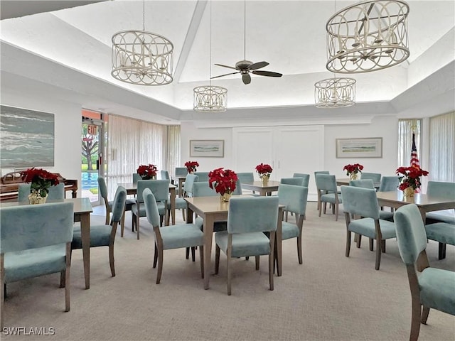 dining area with a tray ceiling, light carpet, and ceiling fan with notable chandelier