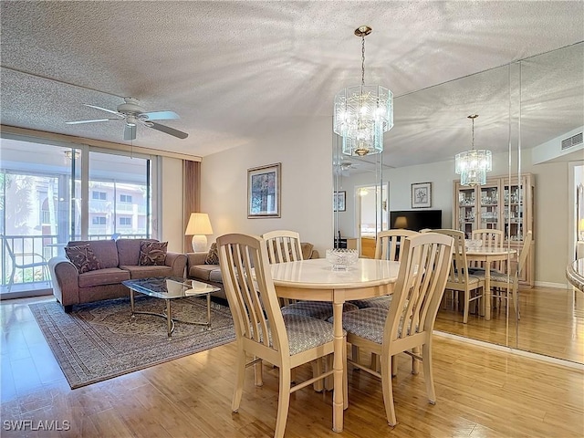 dining room featuring visible vents, ceiling fan with notable chandelier, a textured ceiling, and light wood-style floors