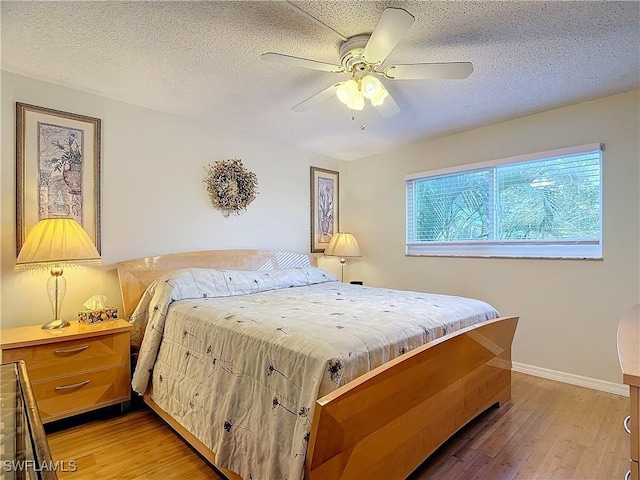 bedroom with ceiling fan, baseboards, light wood finished floors, and a textured ceiling