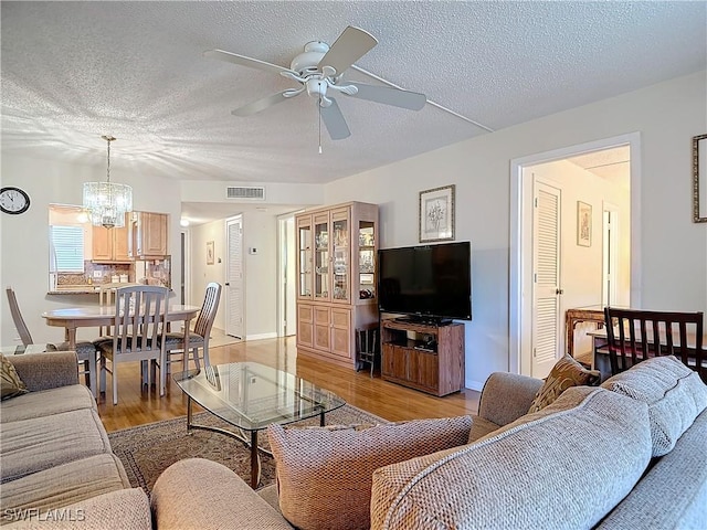 living area featuring light wood-type flooring, visible vents, a textured ceiling, and ceiling fan with notable chandelier