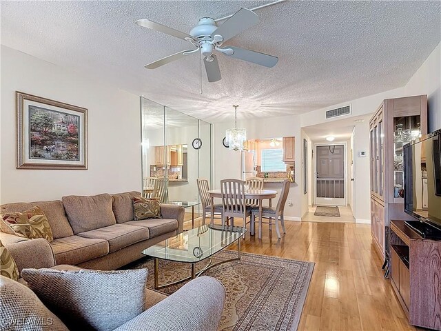 living area featuring visible vents, light wood-style flooring, a textured ceiling, and ceiling fan with notable chandelier