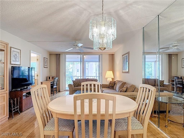 dining area featuring ceiling fan with notable chandelier, light wood-type flooring, and a textured ceiling