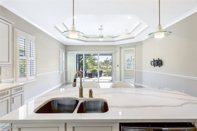 kitchen featuring light stone counters, a tray ceiling, crown molding, sink, and pendant lighting