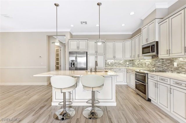 kitchen with appliances with stainless steel finishes, sink, pendant lighting, light hardwood / wood-style floors, and an island with sink