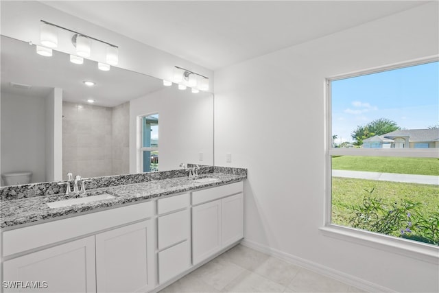 bathroom with a tile shower, plenty of natural light, vanity, and toilet