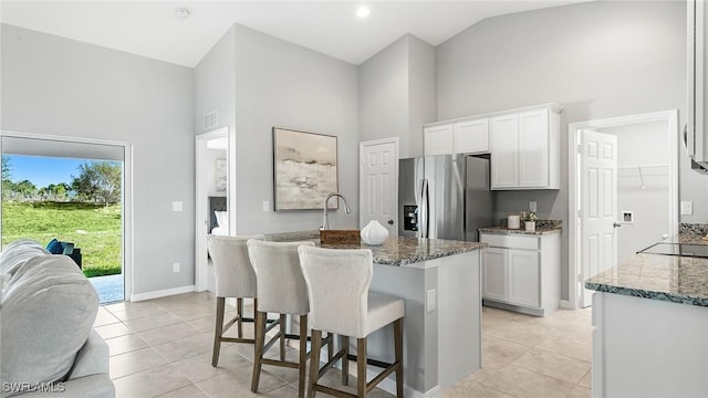 kitchen with stainless steel fridge with ice dispenser, white cabinets, a kitchen island with sink, and stone countertops