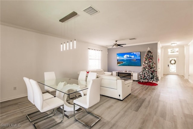 dining space featuring light hardwood / wood-style floors, ceiling fan with notable chandelier, and ornamental molding