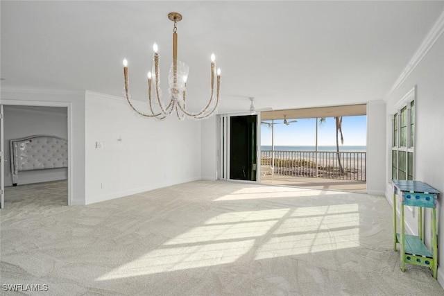 unfurnished room featuring a notable chandelier, a water view, ornamental molding, and light carpet