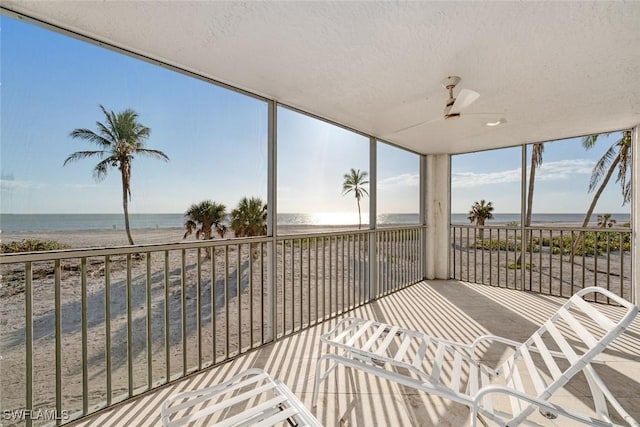 sunroom featuring ceiling fan, a water view, and a beach view