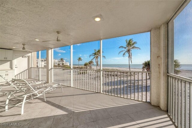 view of patio with ceiling fan, a water view, a balcony, and a view of the beach