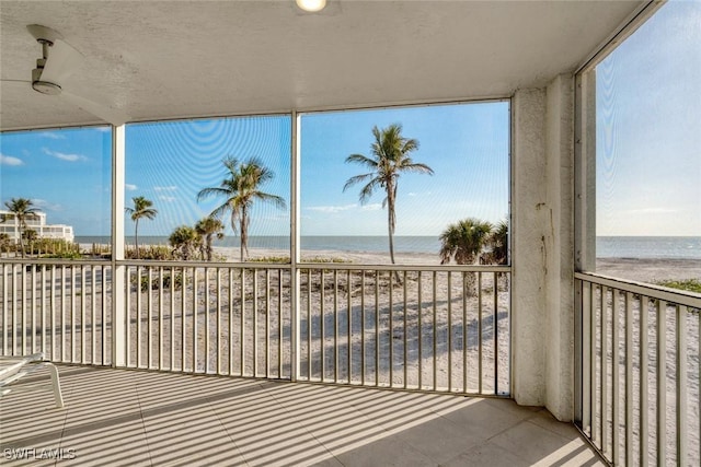 unfurnished sunroom with a water view, a beach view, and a wealth of natural light