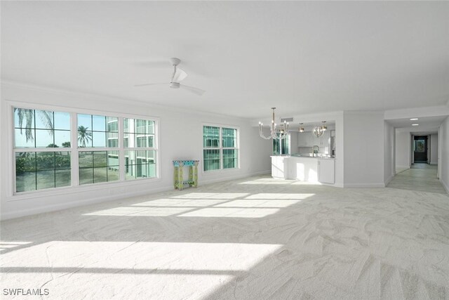 unfurnished living room with ceiling fan with notable chandelier, ornamental molding, and light carpet