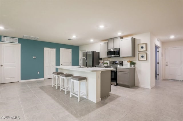 kitchen featuring gray cabinetry, stainless steel appliances, a kitchen island with sink, and a breakfast bar area