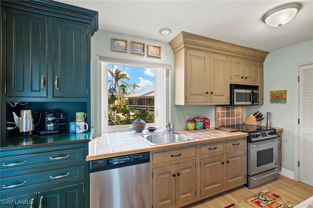 kitchen with tile countertops, sink, light hardwood / wood-style floors, and appliances with stainless steel finishes