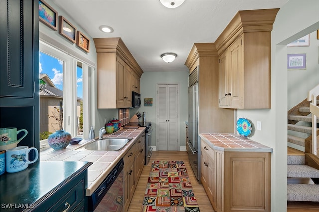 kitchen with tile countertops, sink, black appliances, and light hardwood / wood-style flooring