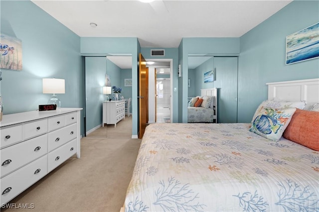 bedroom with two closets, ensuite bath, ceiling fan, and light colored carpet