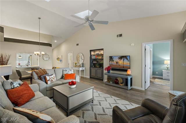 living room with ceiling fan with notable chandelier, light hardwood / wood-style floors, and high vaulted ceiling