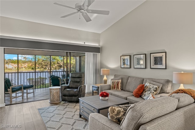 living room featuring high vaulted ceiling, light hardwood / wood-style flooring, ceiling fan, and a water view