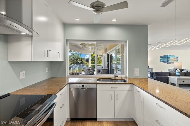 kitchen with decorative light fixtures, stainless steel appliances, wall chimney range hood, white cabinetry, and ceiling fan