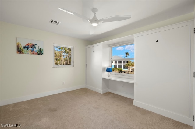 unfurnished bedroom featuring built in desk, light carpet, and ceiling fan