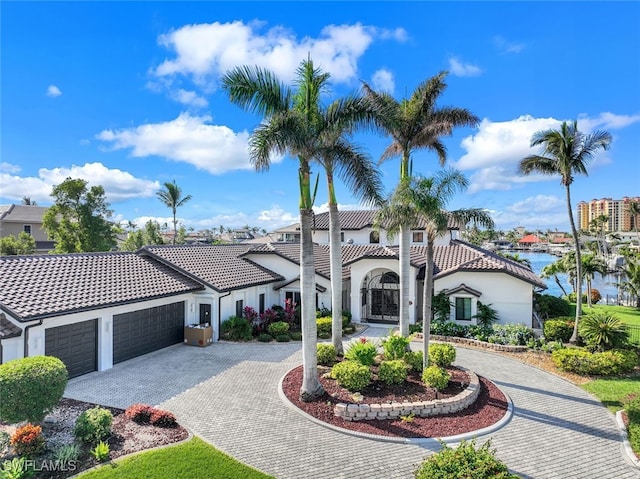 mediterranean / spanish home featuring a water view, a tile roof, a garage, and curved driveway