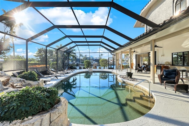 pool featuring ceiling fan, glass enclosure, a bar, and a patio area