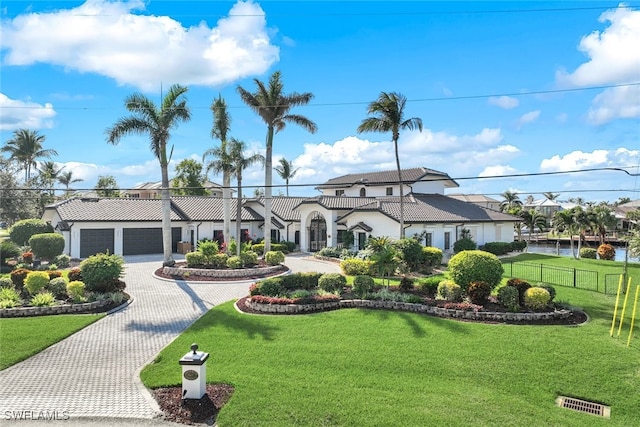 mediterranean / spanish-style house featuring a garage, a water view, fence, decorative driveway, and a front lawn