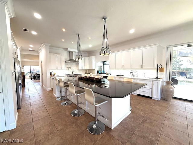 kitchen featuring wall chimney range hood, a breakfast bar area, white cabinetry, and a center island