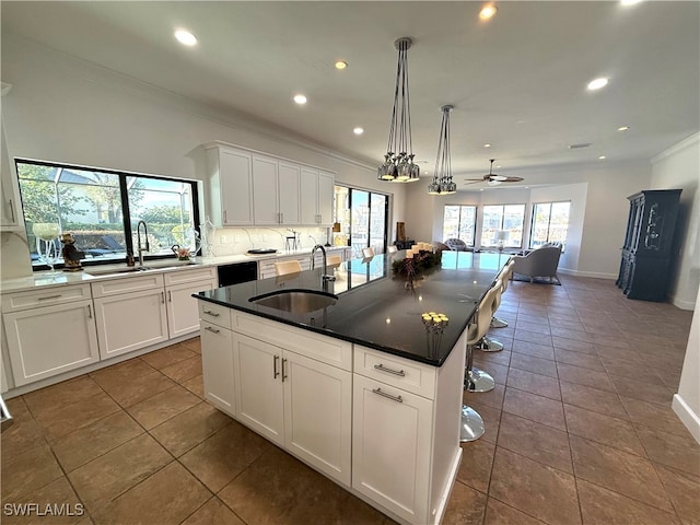 kitchen featuring dark countertops, a center island with sink, white cabinets, and a sink