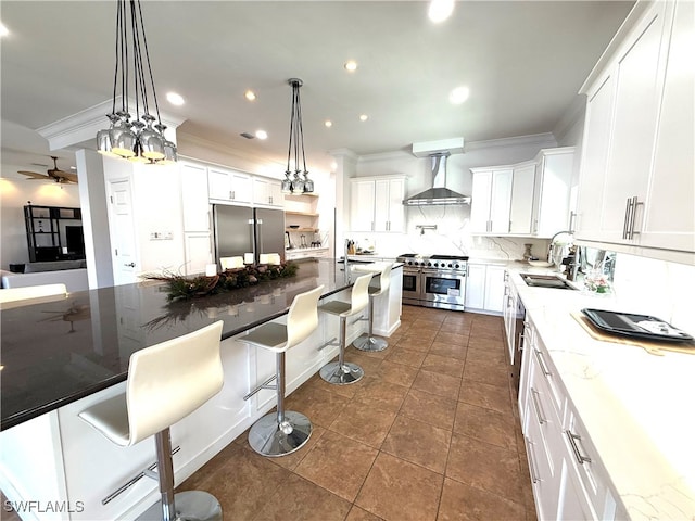 kitchen with premium appliances, pendant lighting, white cabinets, wall chimney range hood, and light stone countertops