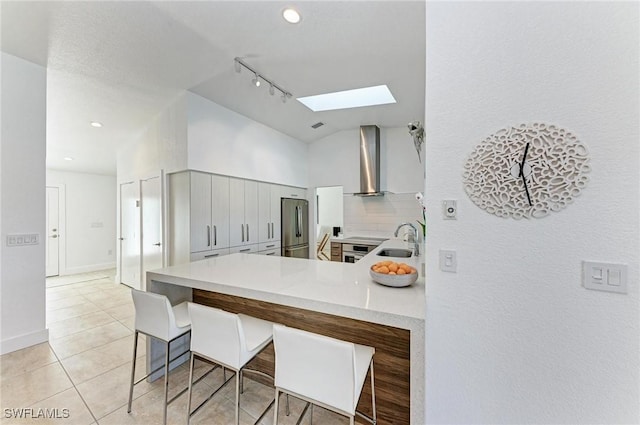 kitchen with kitchen peninsula, wall chimney exhaust hood, lofted ceiling with skylight, sink, and stainless steel refrigerator