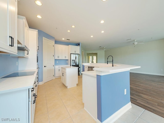 kitchen with a center island with sink, ceiling fan, light wood-type flooring, appliances with stainless steel finishes, and white cabinetry