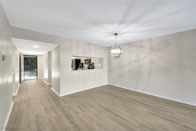 unfurnished room with light hardwood / wood-style floors, an inviting chandelier, and sink