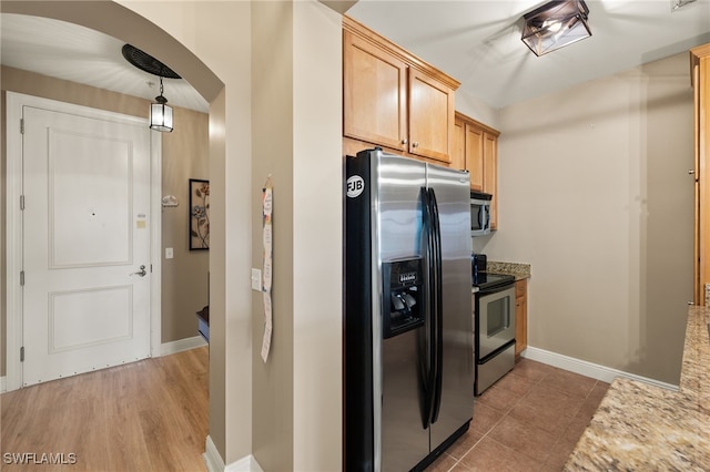kitchen featuring baseboards, light countertops, arched walkways, hanging light fixtures, and stainless steel appliances