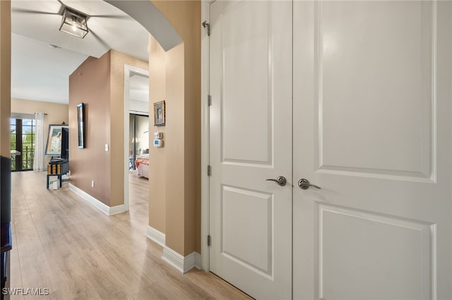 hallway featuring arched walkways, baseboards, and light wood finished floors