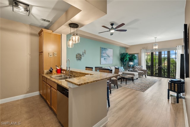 kitchen with a ceiling fan, light stone countertops, dishwasher, a sink, and a peninsula