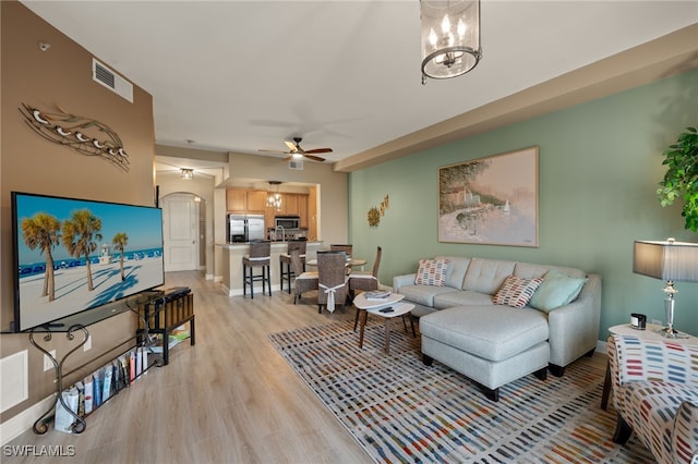 living area featuring visible vents, arched walkways, baseboards, ceiling fan with notable chandelier, and light wood finished floors