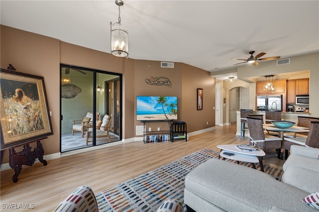 living room with visible vents, arched walkways, baseboards, ceiling fan with notable chandelier, and light wood-style floors