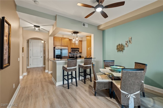 dining space featuring visible vents, baseboards, ceiling fan, arched walkways, and light wood finished floors